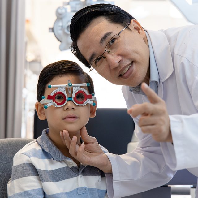 Eye doctor testing child’s vision with phoropter